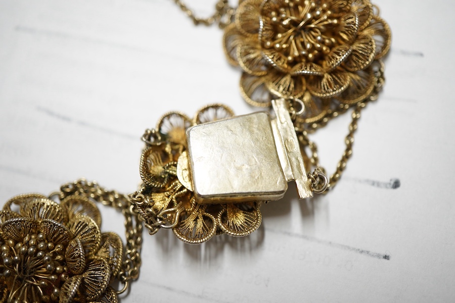 A gilt white metal filigree parure, comprising a necklace, 36cm, with flower head motifs, a pair of flower head earrings and a bracelet.
